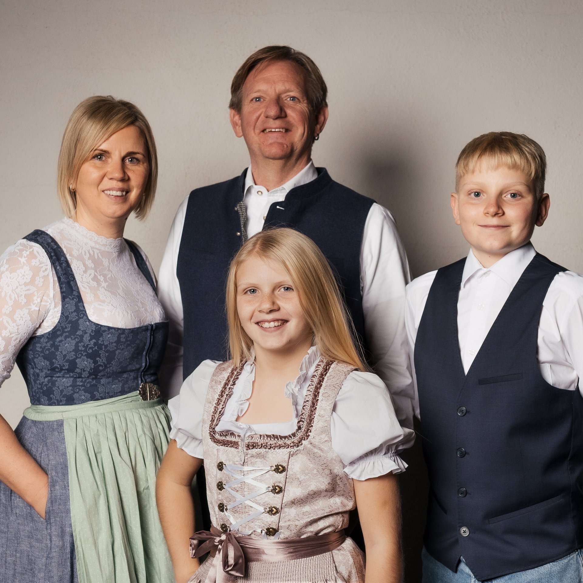 Familienfreude im Hirschen Wohlfühlhotel Familie in traditioneller Tracht posiert zusammen vor neutralem Hintergrund bei einem Hotel.